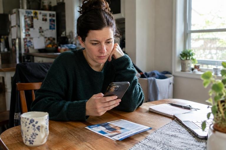 Woman using a smartphone at her kitchen table, illustrating the importance of understanding customer search intent.