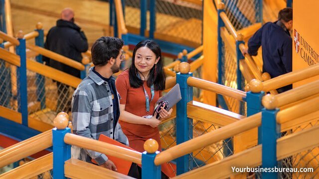Two university students having a conversation on a staircase inside a modern University of Cambridge building.